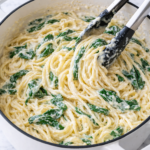 Creamy lemon ricotta pasta with spinach being tossed with tongs in a white Dutch oven