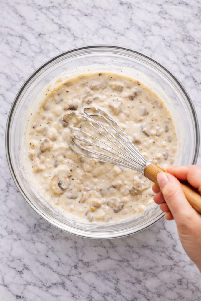 Creamy onion soup mixture being whisked in a glass bowl on a marble countertop