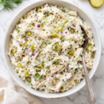 creamy pickle chicken salad with dill pickles and red onion in white bowl on marble counter