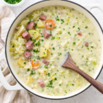 Creamy potato and Swiss cheese soup with corned beef and cabbage in a white Dutch oven with dark wood spoon