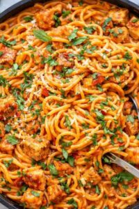 Creamy roasted red pepper chicken pasta with spaghetti, tender seasoned chicken, fresh basil, and grated parmesan cheese