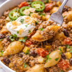 creamy taco pasta bowl with fork scoop sour cream tortilla chips and cilantro