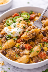 creamy taco pasta bowl with fork scoop sour cream tortilla chips and cilantro
