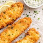 crispy beer battered fish fry with homemade tartar sauce and lemon slices on parchment paper