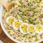 dill pickle deviled egg pasta salad with ham topped with sliced eggs dill and black pepper in a white bowl on a marble counter