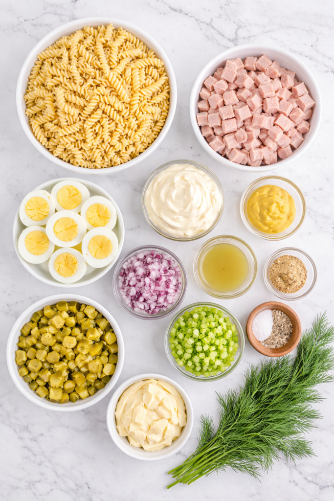 flat lay of ingredients for dill pickle deviled egg pasta salad with ham on a marble counter