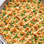 Easy chicken fried rice in a silver skillet drizzled with spicy mayo, made with tender chicken, peas, carrots, and green onions.