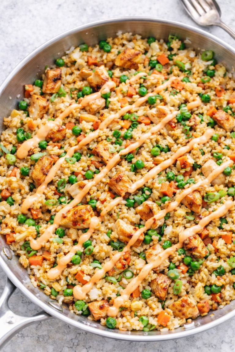 Easy chicken fried rice in a silver skillet drizzled with spicy mayo, made with tender chicken, peas, carrots, and green onions.