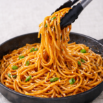 easy hibachi noodles lifted with tongs in skillet with garlic butter soy sauce