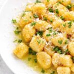 Easy homemade potato gnocchi tossed in butter with parmesan cheese and fresh parsley in a white bowl on a marble counter