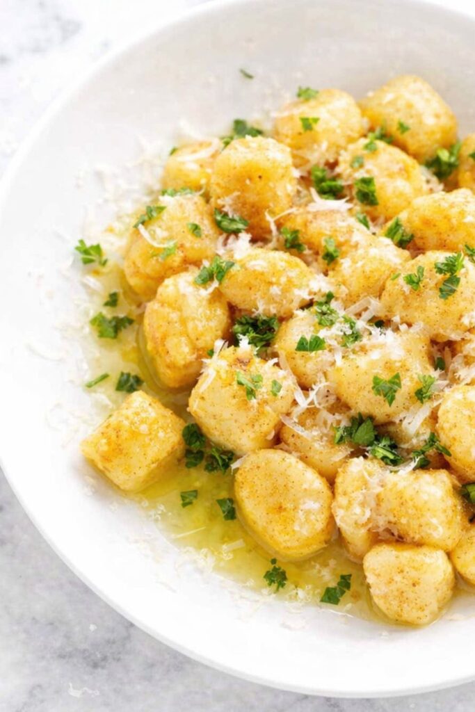 Easy homemade potato gnocchi tossed in butter with parmesan cheese and fresh parsley in a white bowl on a marble counter