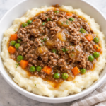 French onion ground beef mashed potato bowl with peas and carrots under savory onion gravy served in a white bowl