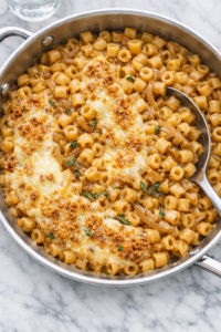 creamy french onion pasta with ditalini in beef broth sauce topped with melted gruyere and toasted breadcrumbs in stainless skillet