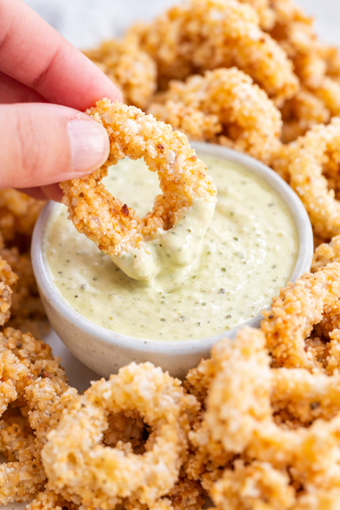 Hand dipping crispy fried calamari ring into creamy garlic aioli sauce