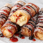 crispy fried cheesecake egg rolls drizzled with strawberry syrup and chocolate syrup on a white plate with powdered sugar