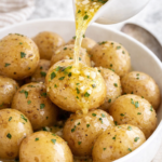 Baby salt potatoes in a white bowl with melted garlic butter being poured over top
