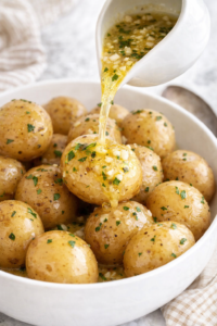 Baby salt potatoes in a white bowl with melted garlic butter being poured over top
