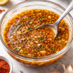 Glass bowl of garlic butter seafood boil sauce with minced garlic, Cajun spices, and hot sauce on a marble countertop.
