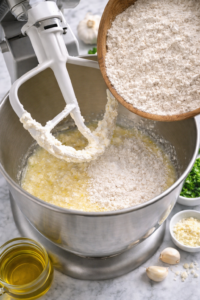 dry ingredients being added to wet ingredients in stand mixer bowl for garlic cottage cheese bread