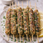 Greek spinach and feta chicken kabobs baked on skewers with parsley and lemon slices on a white plate