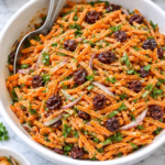 green goddess carrot slaw with dried cranberries and herbs tossed in creamy dressing in a white bowl on marble counter