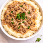 ground beef stroganoff served over mashed potatoes in a white bowl with creamy mushroom gravy