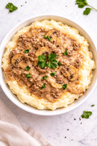 ground beef stroganoff served over mashed potatoes in a white bowl with creamy mushroom gravy