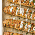 Oven-baked ground chicken shawarma kabobs drizzled with creamy garlic yogurt sauce on a parchment-lined sheet pan.
