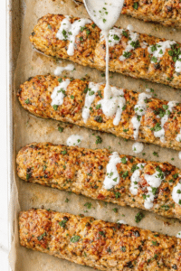 Oven-baked ground chicken shawarma kabobs drizzled with creamy garlic yogurt sauce on a parchment-lined sheet pan.