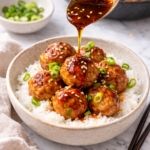 Gyoza meatballs served over steamed rice with soy ginger sauce being spooned over the top, garnished with green onions and sesame seeds on a marble countertop