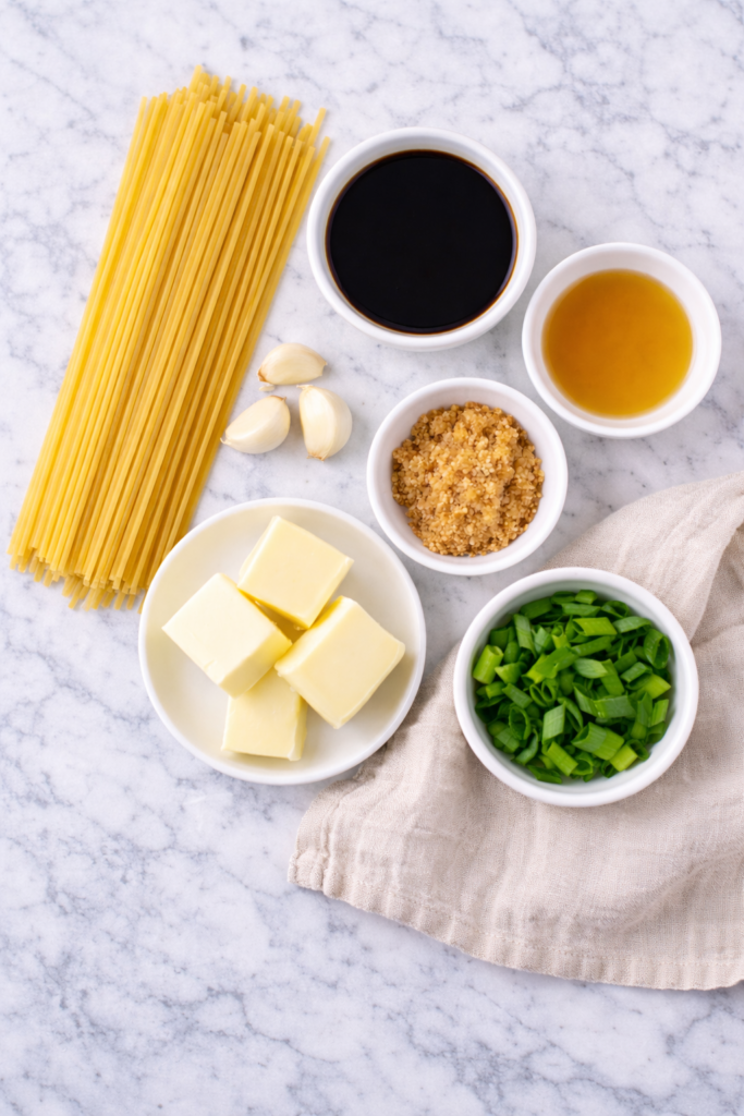 flat lay of hibachi noodle ingredients including spaghetti garlic butter soy sauce sesame oil brown sugar and green onions on marble counter