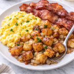 crispy home fries with creamy scrambled eggs and bacon on white plate with fork