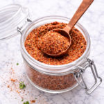 Homemade Cajun seasoning spice blend in a glass jar with a copper spoon on a marble countertop