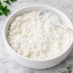 Homemade cottage cheese in a white bowl on a marble countertop with fresh herbs nearby
