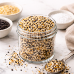 Homemade everything bagel seasoning in a glass jar with sesame seeds, poppy seeds, garlic, onion, and salt on a marble countertop