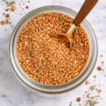 Birds eye view of homemade guacamole seasoning spice blend in a glass jar with a spoon on a white marble countertop
