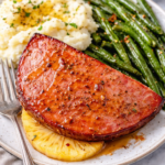 Hot honey glazed ham steak with pineapple served with mashed potatoes and green beans on a plate