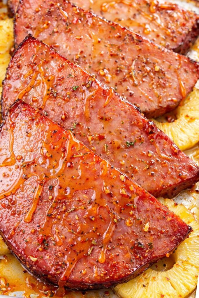 Hot honey glazed ham steaks roasted with pineapple slices on a sheet pan on a marble countertop