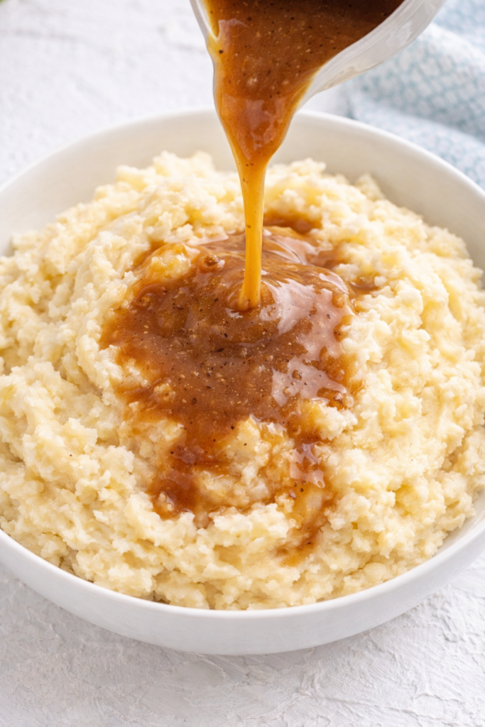 Instant mashed potatoes in a white bowl with brown gravy being poured over the top