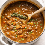 Classic Irish lamb stew with peas and fresh thyme in a white enamel Dutch oven