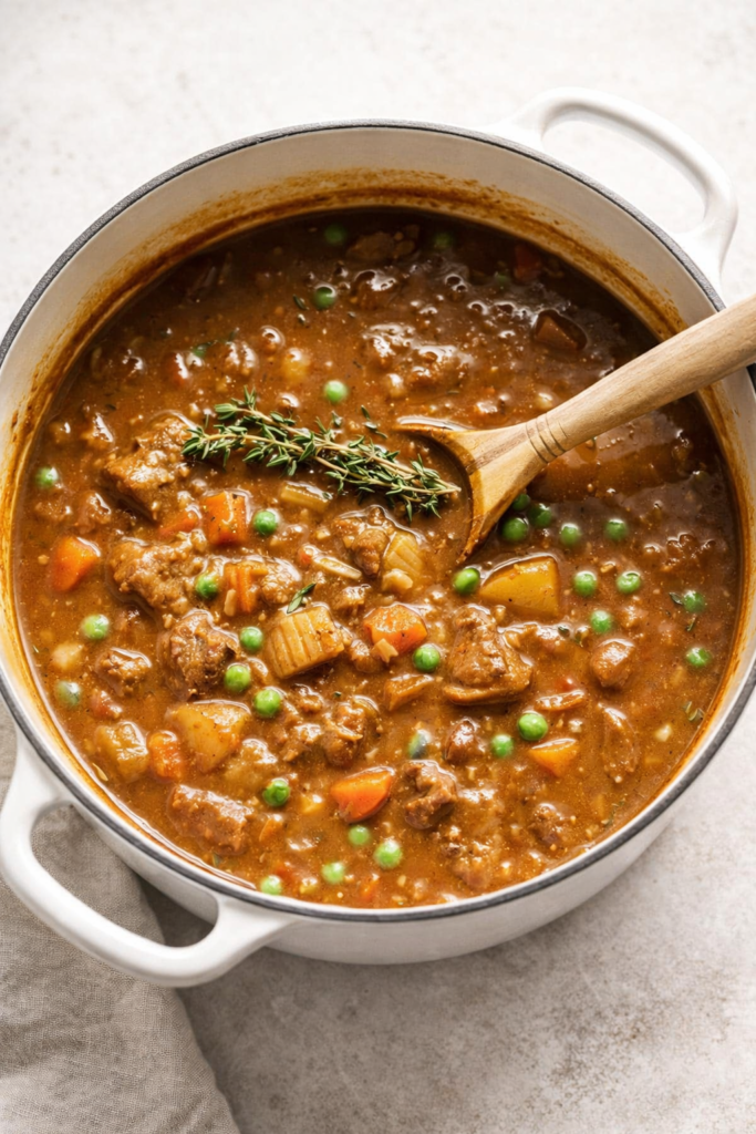Classic Irish lamb stew with peas and fresh thyme in a white enamel Dutch oven