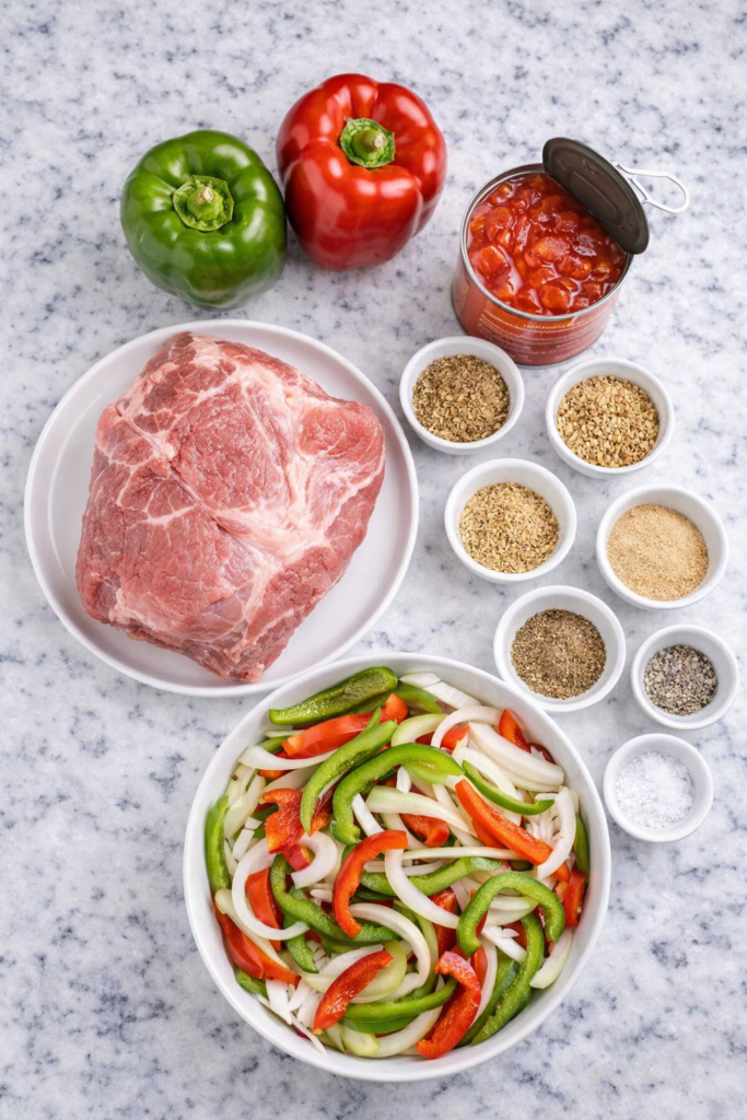 Ingredients for Italian pulled pork including pork roast, peppers, onions, diced tomatoes, and spices on marble counter