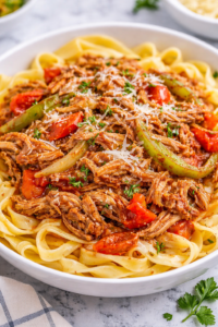 Italian pulled pork with peppers and onions served over fettuccine pasta in a white bowl