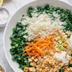 Kale and carrot Caesar salad with shaved carrots, Parmesan cheese, croutons, and creamy Caesar dressing in a white bowl on a marble counter