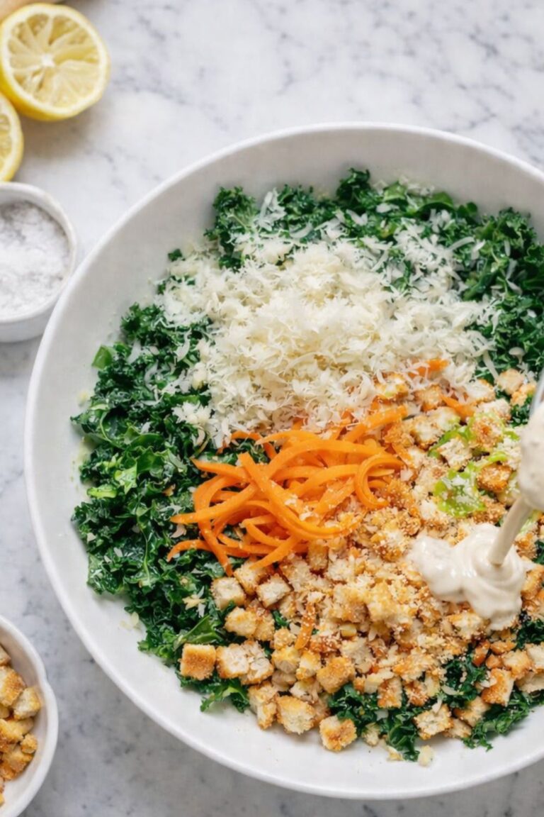 Kale and carrot Caesar salad with shaved carrots, Parmesan cheese, croutons, and creamy Caesar dressing in a white bowl on a marble counter