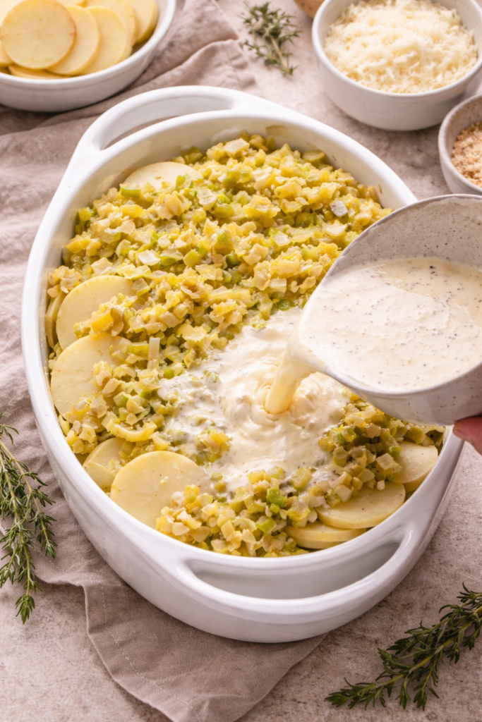 Layering potatoes and leeks in a baking dish while pouring cream mixture for potato and leek gratin