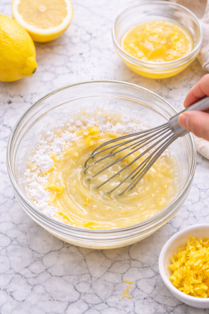 Whisking fresh lemon juice and powdered sugar in a glass bowl to make lemon glaze for lemon poppy seed cornmeal cake