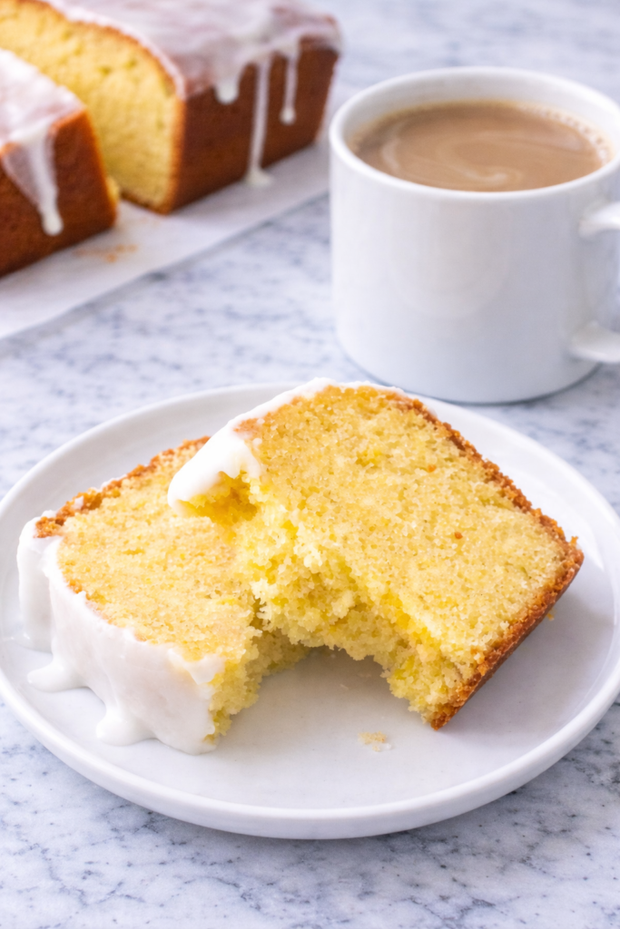 Slice of lemon loaf cake on a white plate with creamy coffee