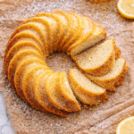 Lemon poppy seed cornmeal bundt cake with lemon glaze on brown wrinkled parchment paper over marble countertop, dusted with powdered sugar and scattered poppy seeds