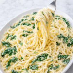 Creamy lemon ricotta pasta with spinach on a large white oval platter on a marble counter with a fork twirling the noodles